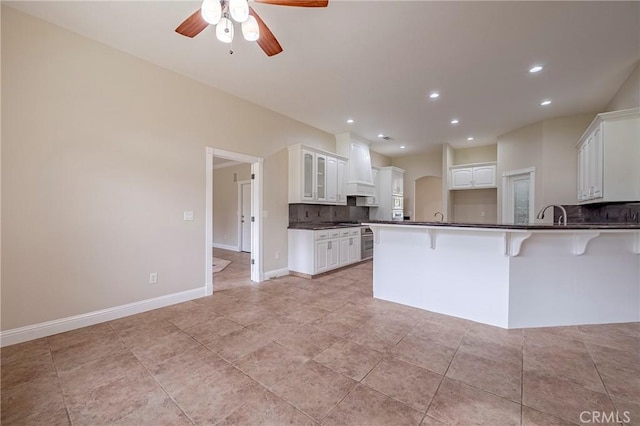 kitchen with backsplash, custom range hood, white cabinets, a kitchen bar, and kitchen peninsula