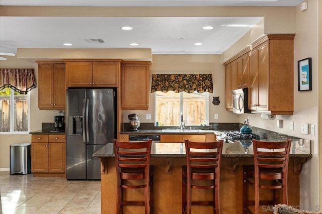 kitchen featuring stainless steel appliances, a kitchen bar, sink, and dark stone counters