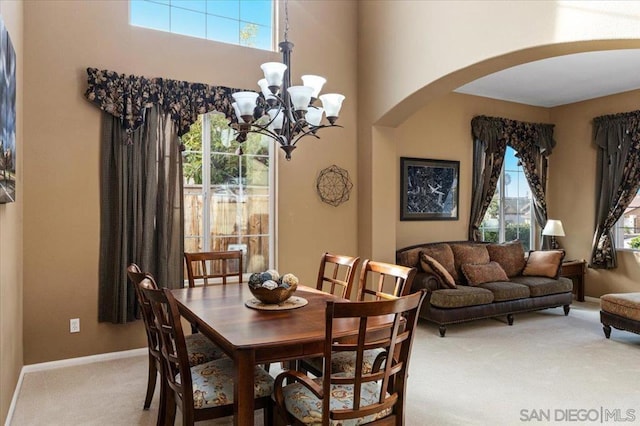 dining space featuring light carpet, a towering ceiling, a wealth of natural light, and an inviting chandelier