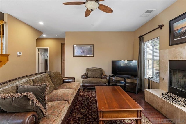 living room with a tiled fireplace, dark hardwood / wood-style floors, and ceiling fan