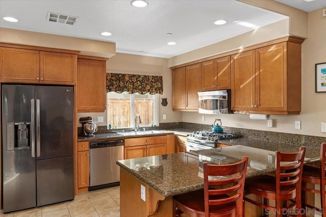 kitchen with sink, dark stone countertops, a kitchen bar, kitchen peninsula, and stainless steel appliances