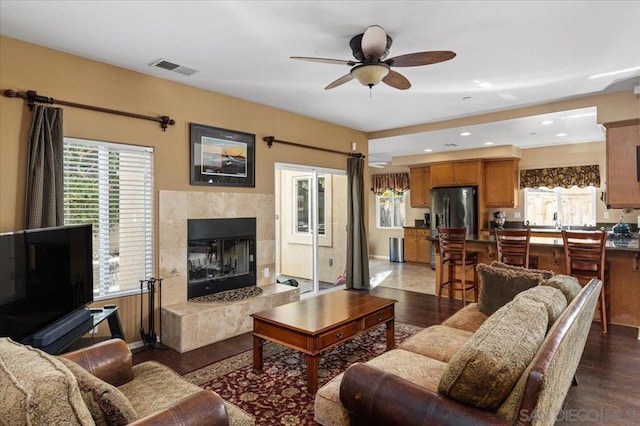 living room with ceiling fan, dark hardwood / wood-style floors, a tile fireplace, and a wealth of natural light