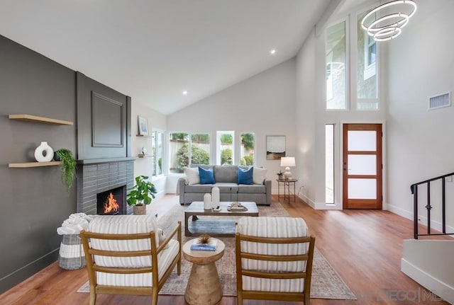 living room with a brick fireplace, high vaulted ceiling, and light hardwood / wood-style floors