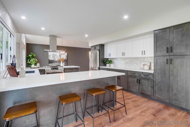 kitchen with a kitchen bar, decorative light fixtures, premium appliances, kitchen peninsula, and wall chimney range hood