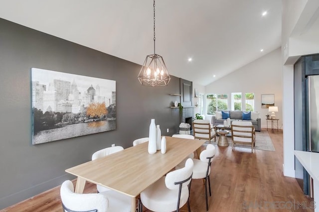 dining room with hardwood / wood-style flooring, a fireplace, and high vaulted ceiling