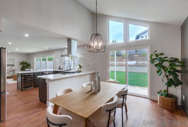 dining area with high vaulted ceiling, an inviting chandelier, beverage cooler, and light wood-type flooring