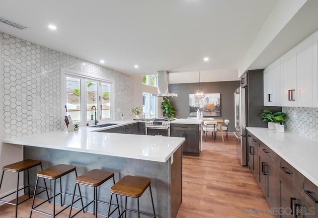 kitchen featuring wall chimney exhaust hood, a breakfast bar area, kitchen peninsula, pendant lighting, and white cabinets