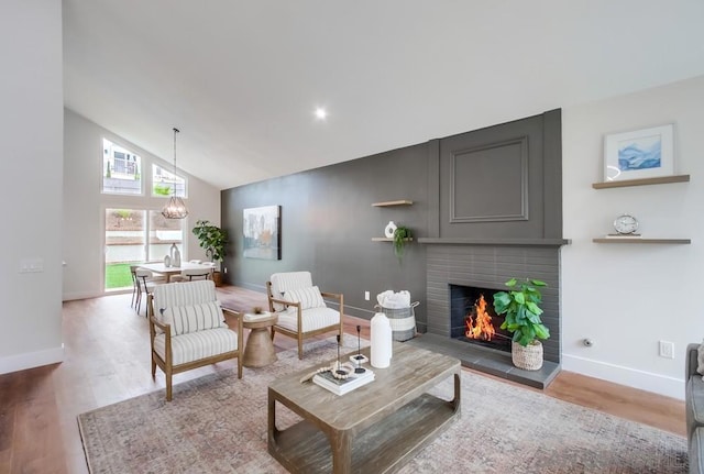 living room with a brick fireplace, hardwood / wood-style floors, a chandelier, and high vaulted ceiling