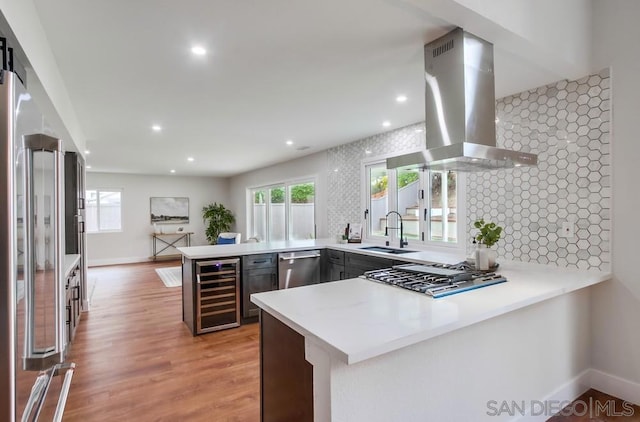 kitchen featuring wine cooler, island exhaust hood, kitchen peninsula, and sink