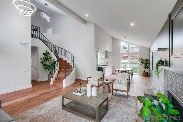 living room featuring a notable chandelier, light hardwood / wood-style flooring, a fireplace, and high vaulted ceiling