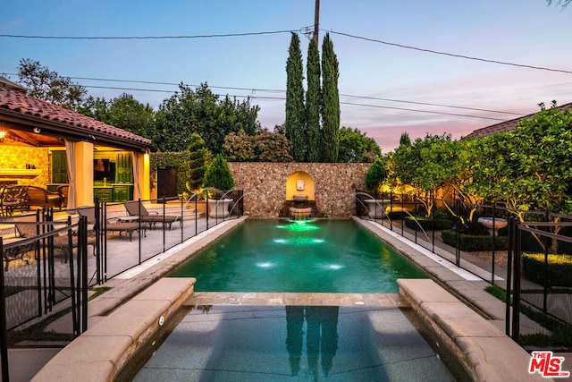 pool at dusk with a patio, pool water feature, and a fireplace