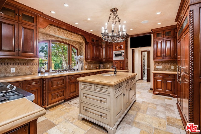 kitchen featuring stainless steel microwave, decorative light fixtures, sink, decorative backsplash, and a kitchen island with sink