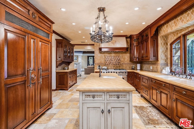 kitchen with sink, a center island with sink, ornamental molding, custom range hood, and backsplash