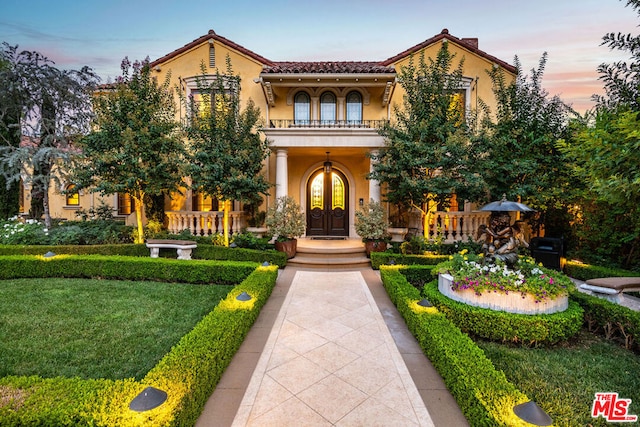 mediterranean / spanish-style home featuring french doors, a balcony, and a lawn