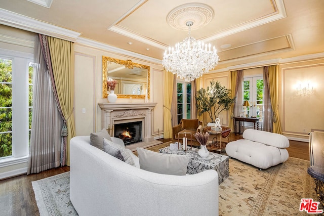 living room with hardwood / wood-style floors, a fireplace, ornamental molding, a tray ceiling, and an inviting chandelier