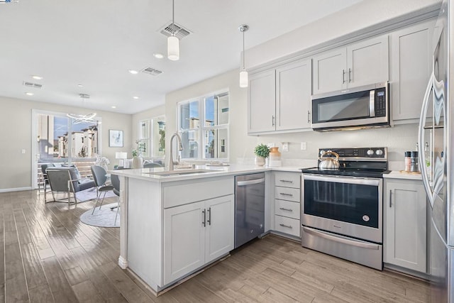 kitchen featuring sink, light wood-type flooring, kitchen peninsula, pendant lighting, and stainless steel appliances