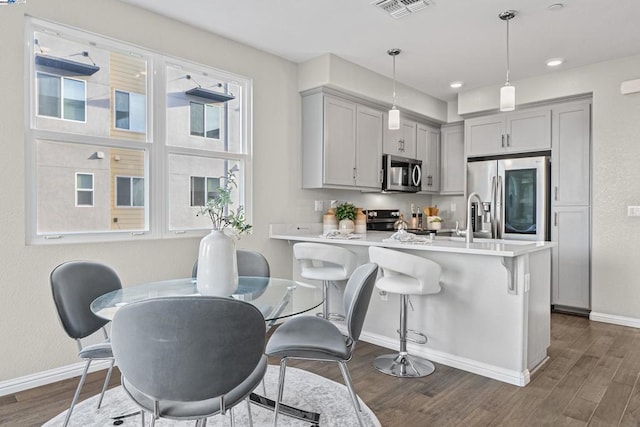 kitchen featuring gray cabinets, stainless steel appliances, a kitchen bar, dark hardwood / wood-style flooring, and decorative light fixtures