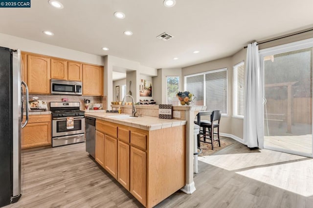 kitchen featuring sink, decorative backsplash, tile counters, stainless steel appliances, and a center island with sink