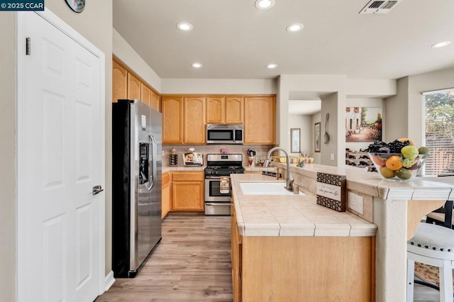 kitchen with light brown cabinetry, sink, tile countertops, appliances with stainless steel finishes, and kitchen peninsula