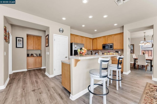 kitchen featuring pendant lighting, appliances with stainless steel finishes, a kitchen breakfast bar, light hardwood / wood-style floors, and decorative backsplash