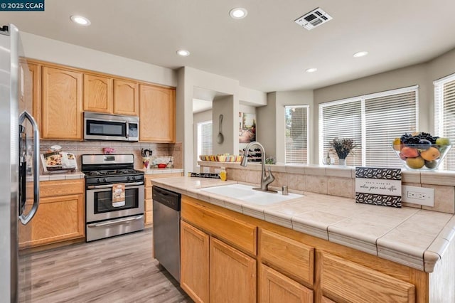 kitchen with sink, light hardwood / wood-style flooring, backsplash, stainless steel appliances, and tile countertops