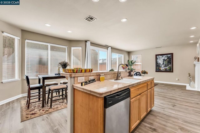 kitchen with sink, tile countertops, stainless steel dishwasher, an island with sink, and light hardwood / wood-style floors