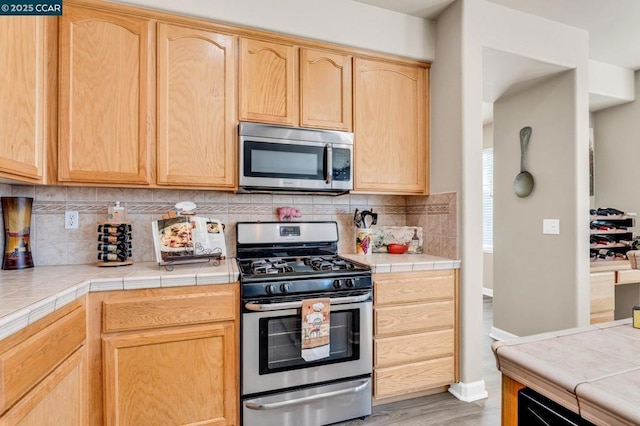 kitchen with backsplash, tile counters, stainless steel appliances, and light brown cabinets