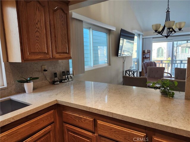 kitchen featuring tasteful backsplash, light stone counters, a chandelier, vaulted ceiling, and hanging light fixtures