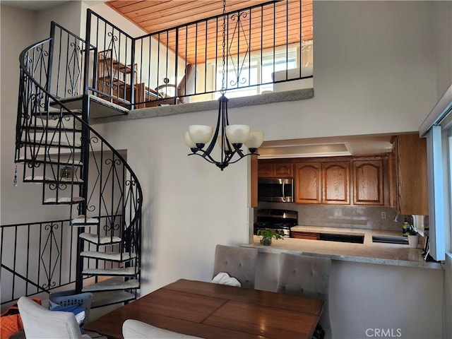 kitchen with sink, a notable chandelier, a towering ceiling, stainless steel appliances, and backsplash