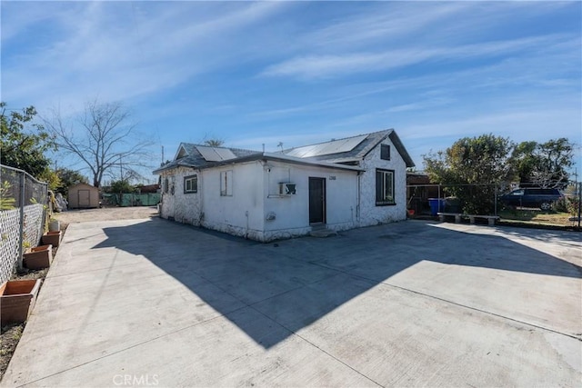 view of side of home with a storage shed, a patio, and solar panels