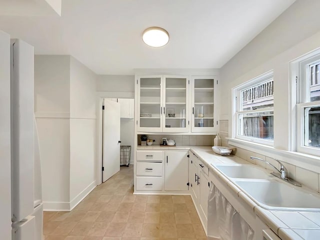 kitchen with white cabinetry, tile countertops, sink, and backsplash