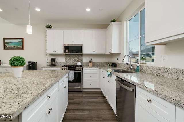 kitchen featuring dark wood finished floors, appliances with stainless steel finishes, hanging light fixtures, white cabinetry, and a sink