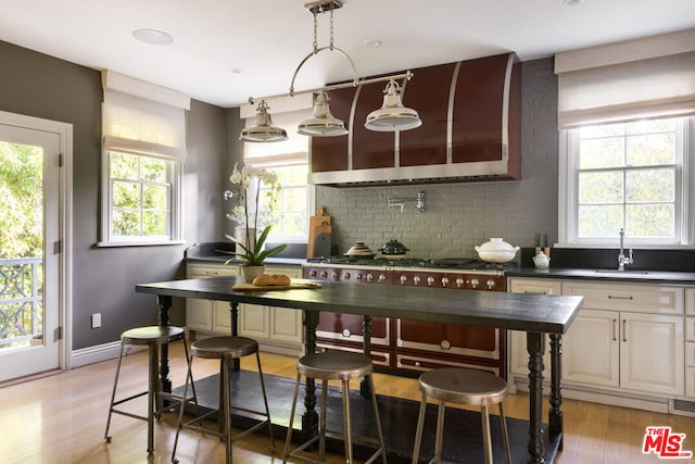 kitchen featuring pendant lighting, tasteful backsplash, sink, stainless steel gas cooktop, and light hardwood / wood-style floors