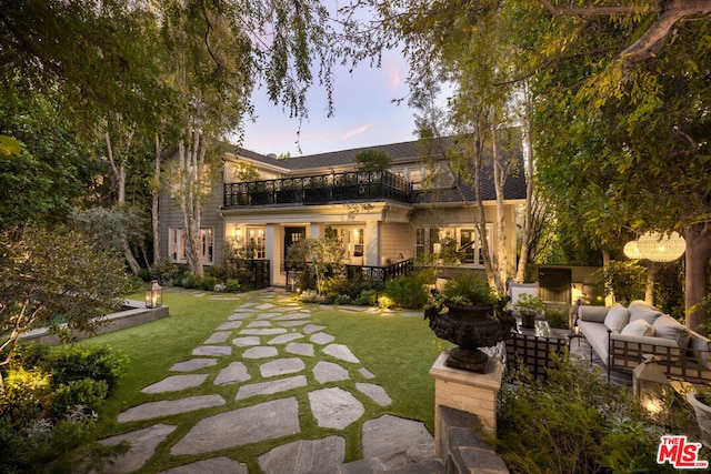 back house at dusk featuring a yard, an outdoor hangout area, a balcony, and a patio area