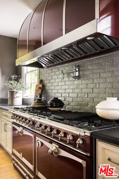 kitchen with range with two ovens, extractor fan, backsplash, and light hardwood / wood-style floors