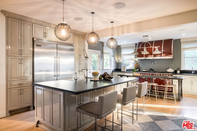 kitchen with cream cabinets, a kitchen breakfast bar, light hardwood / wood-style floors, built in fridge, and a kitchen island with sink