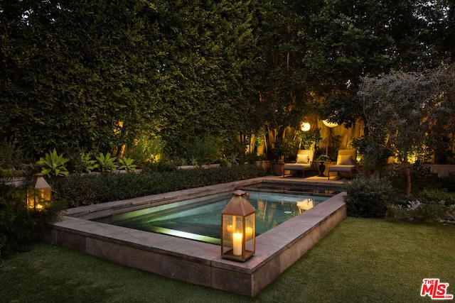 pool at night featuring a yard