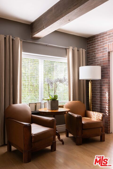 sitting room featuring brick wall, a wealth of natural light, beam ceiling, and light hardwood / wood-style flooring