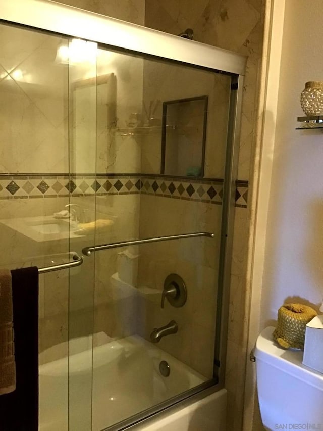 bathroom featuring combined bath / shower with glass door and toilet