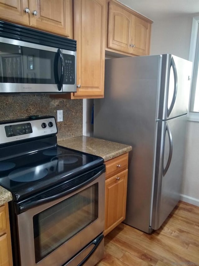 kitchen with stainless steel appliances, tasteful backsplash, light stone counters, and light hardwood / wood-style floors