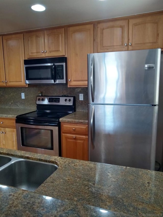 kitchen featuring appliances with stainless steel finishes, sink, backsplash, and dark stone counters