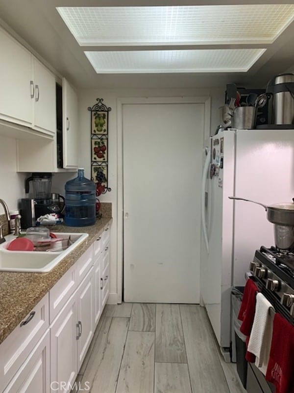 kitchen with sink, white cabinets, white refrigerator, light hardwood / wood-style floors, and gas range