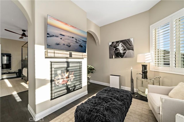 interior space with baseboards, arched walkways, ceiling fan, dark wood-type flooring, and a multi sided fireplace