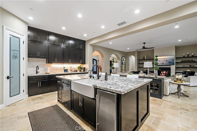 kitchen featuring visible vents, open floor plan, a sink, an island with sink, and dark cabinets