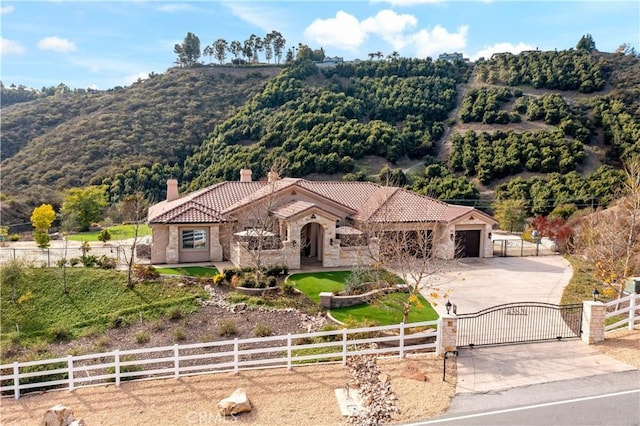 view of front of property featuring a fenced front yard, concrete driveway, a gate, stone siding, and a tiled roof