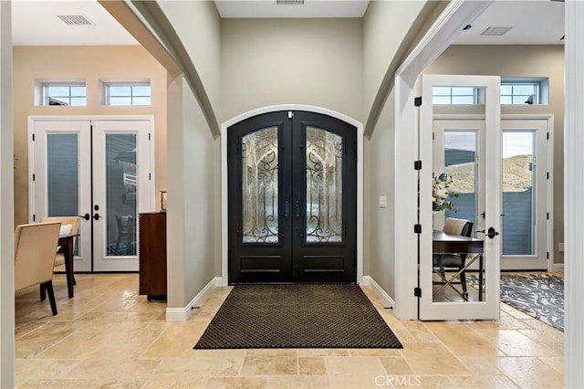 foyer featuring a towering ceiling, arched walkways, stone tile flooring, and french doors