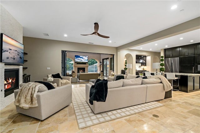 living area featuring arched walkways, a fireplace, stone tile floors, and recessed lighting