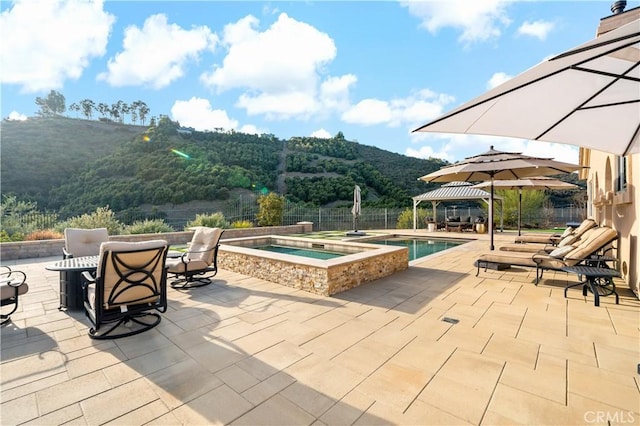 view of patio with a gazebo, fence, a mountain view, and an in ground hot tub