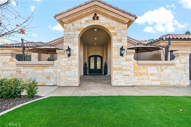 entrance to property with stone siding, a tile roof, a lawn, and stucco siding