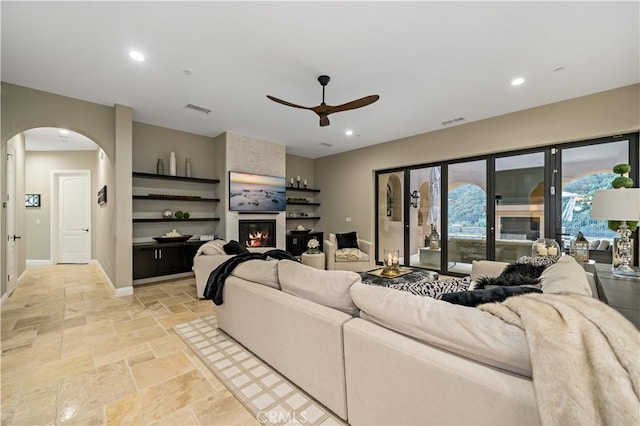 living area with a large fireplace, stone tile floors, visible vents, arched walkways, and baseboards